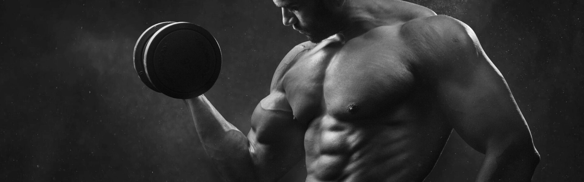 Powerful black and white portrait of a shirtless bodybuilder lifting dumbbells in the gym.